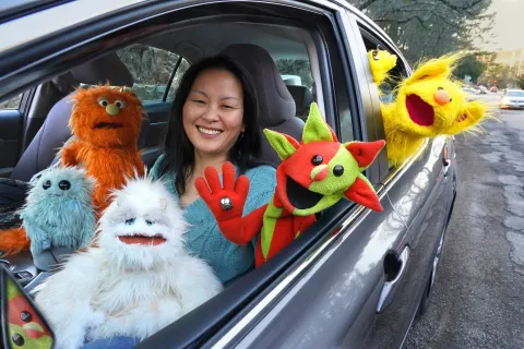 A woman in a car with a lot of puppets around her. Everyone looks very happy.